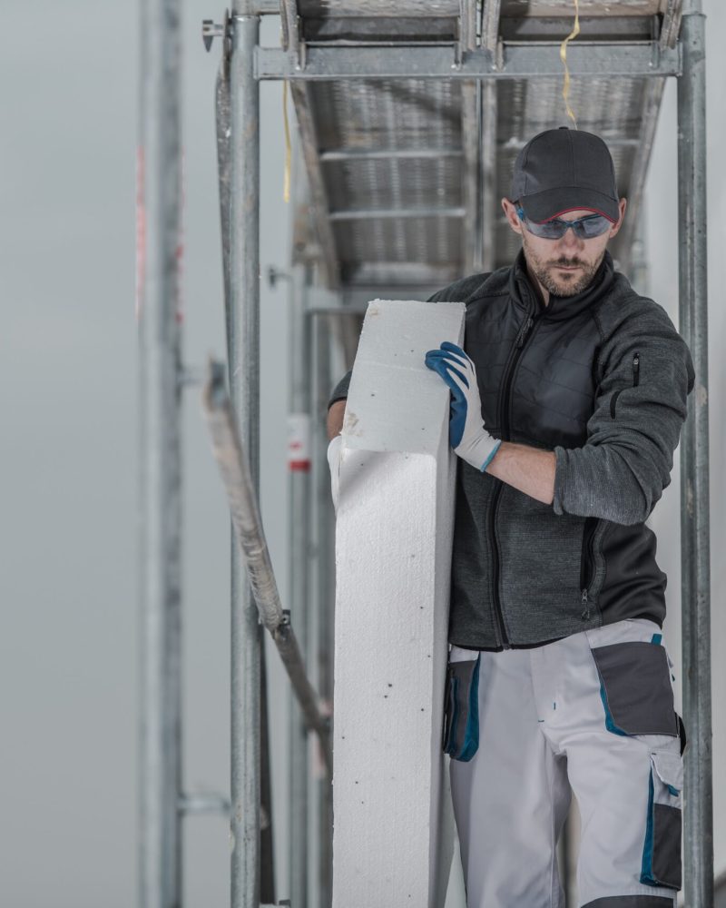 Caucasian Contractor Worker with Piece of Insulation Walking on a Scaffolding.